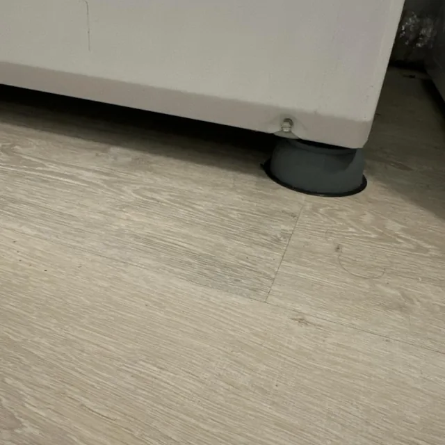 Soporte antivibración colocado bajo la pata de una lavadora en piso laminado